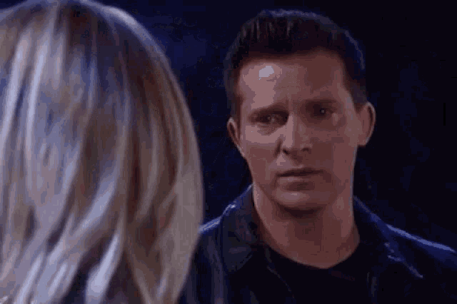 a man and a woman are looking at each other in a dark room . the man is wearing a leather jacket .