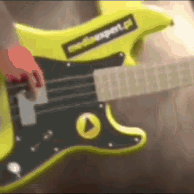 a person is playing a yellow electric guitar with a mediaexpert.pl sticker on it .