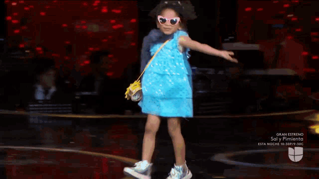 a little girl wearing a blue dress and pink sunglasses dancing on a stage
