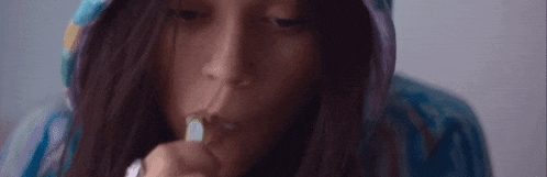 a woman in a hoodie is brushing her teeth with a toothbrush and toothpaste .