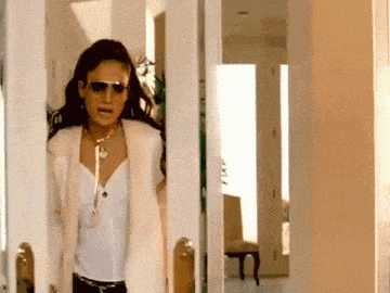 a woman wearing sunglasses and a fur coat is walking through a doorway .
