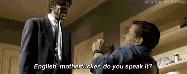 a man in a suit and tie is talking to another man in a kitchen and they are talking about english motherfucker