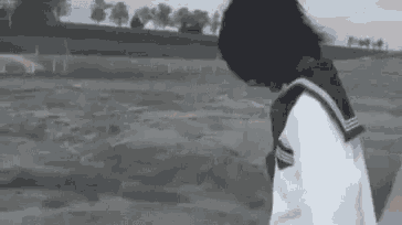a black and white photo of a girl in a school uniform walking on a dirt road .