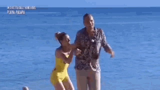 a man and a woman are dancing on a beach . the woman is wearing a yellow bikini .