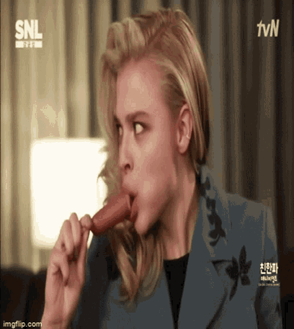 a woman is eating a hot dog with a snl logo in the background