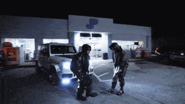two men standing in front of a jp gas station at night
