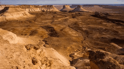 a desert landscape with cliffs and rocks and a body of water in the background