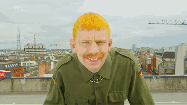 a man with yellow hair and a mustache is wearing a green uniform