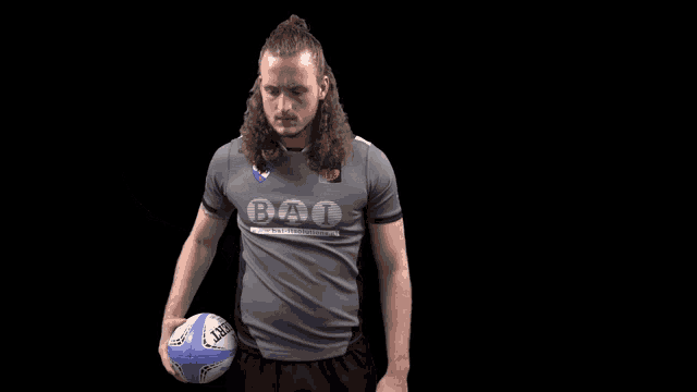 a man wearing a shirt that says bat holds a rugby ball