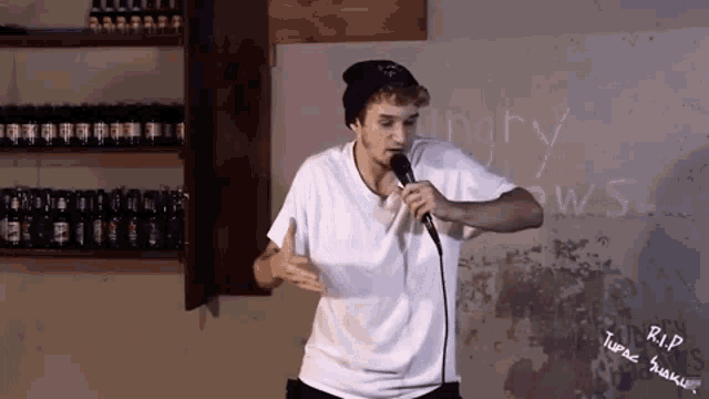 a man singing into a microphone in front of a wall that says rip tupac