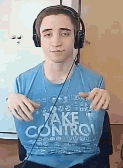 a young man wearing headphones and a blue shirt that says `` take control '' is sitting in front of a white board .