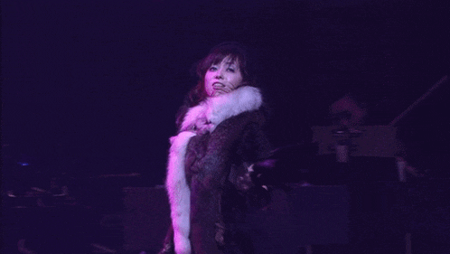 a woman in a fur coat stands on a stage