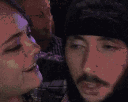 a man and a woman are sitting next to each other at a party . the man is wearing a beanie .
