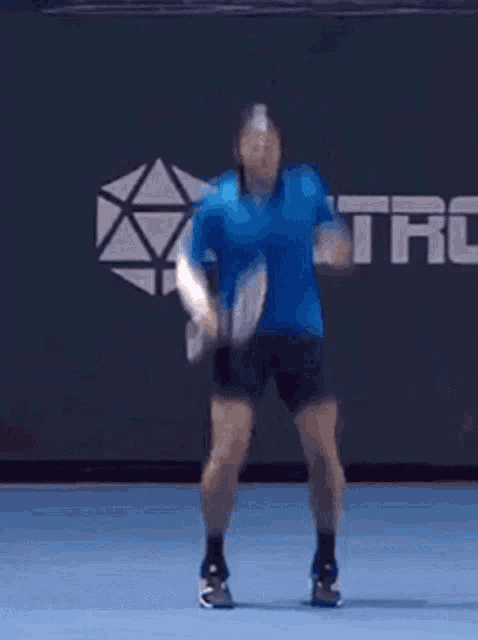 a man in a blue shirt is jumping in the air with a tennis racquet