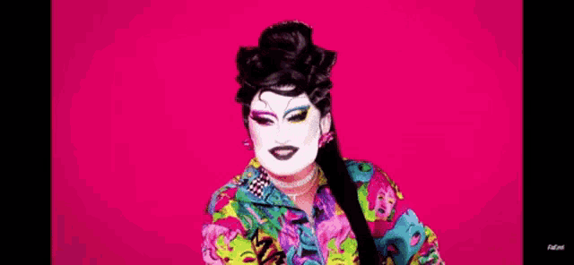 a drag queen is wearing a colorful outfit and a white face paint .