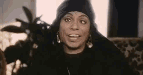 a woman wearing a black scarf and earrings is sitting on a couch and smiling .