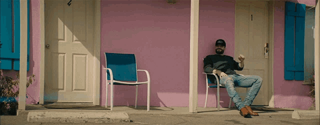 a man sits in a chair in front of a pink building with the number 1 on the door