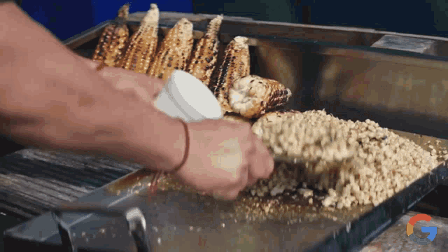a person is cooking corn on the cob with a google logo behind them