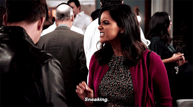 a woman in a pink cardigan is talking to a man in a crowd and says " sneaking "