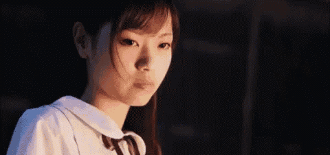 a young girl in a school uniform is looking at the camera in the dark .