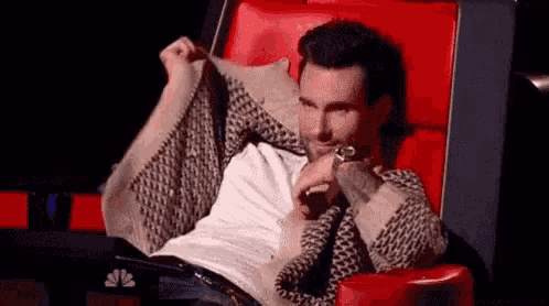 a man is sitting in a red chair holding his sweater over his shoulder .