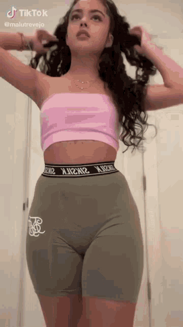a woman in a pink crop top and green shorts is standing in a room .