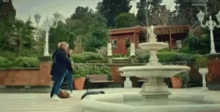 a man and a woman are walking in front of a fountain .