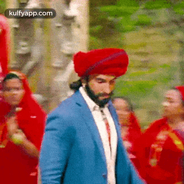a man wearing a blue suit and a red turban is standing in front of a crowd of people .