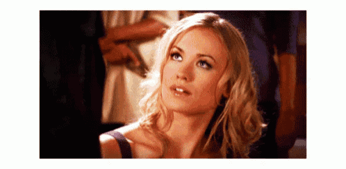 a woman with blonde hair and blue eyes is looking up at something while standing in a crowd .