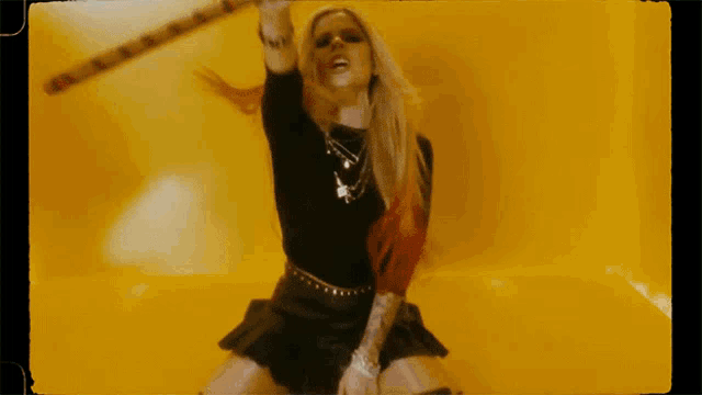 a woman in a black top and black skirt is holding a stick