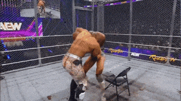 two men are wrestling in a ring with a chair in the middle of the ring .