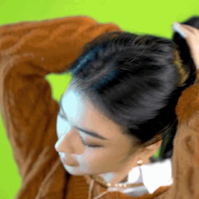 a woman in a brown sweater holds her hair up in a bun