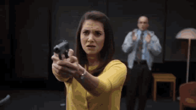 a woman in a yellow sweater is pointing a gun