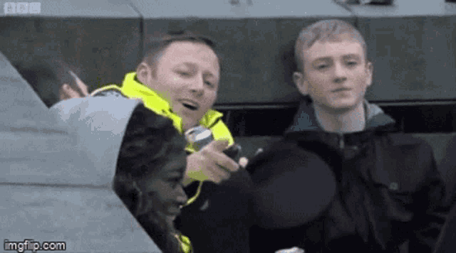 a man in a yellow jacket is talking to another man in a black jacket