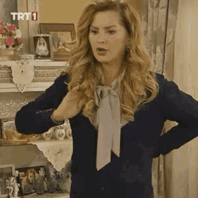 a woman in a blue sweater and a pink tie is standing in a living room with her hands on her hips .
