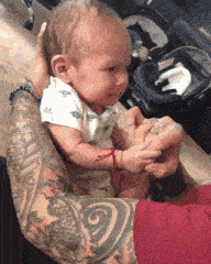 a baby is being held by a man with tattoos