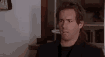 a man in a black suit is making a funny face while sitting in a chair .