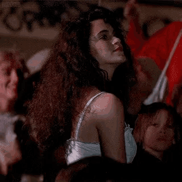 a woman with curly hair is standing in front of a crowd of people and looking at the camera .