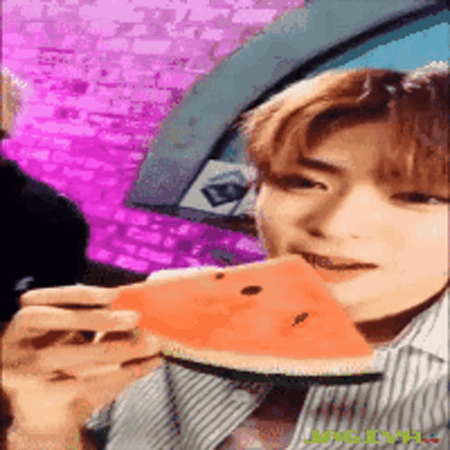 a man is eating a slice of watermelon with a brick wall in the background