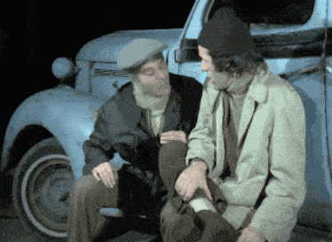 two men are sitting next to a blue car