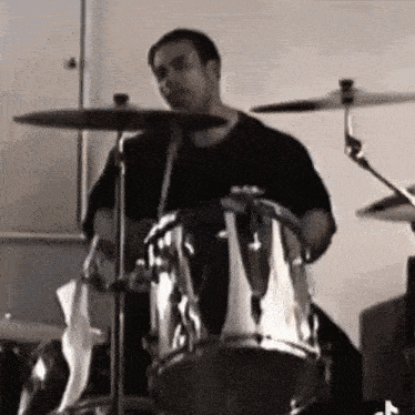 a man in a black shirt is playing a drum set .