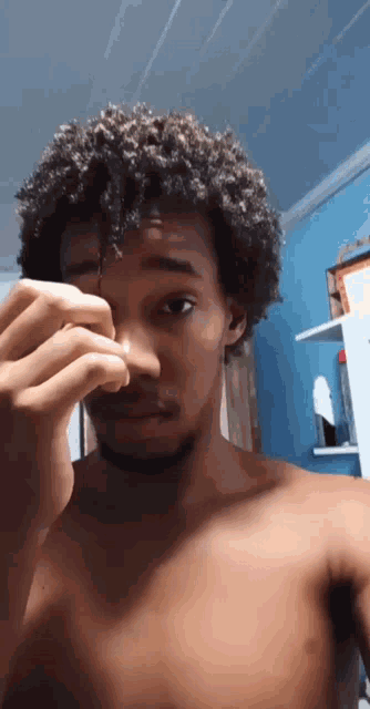 a shirtless man with curly hair holds his nose