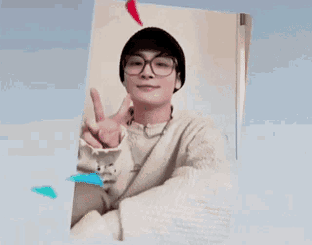 a young man wearing glasses and a hat is making a heart shape with his hands .