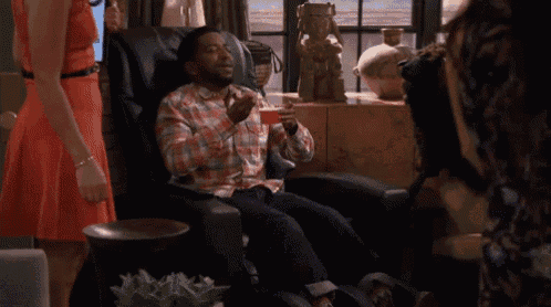 a man is sitting in a chair with a drink in his hand and a woman is standing behind him .