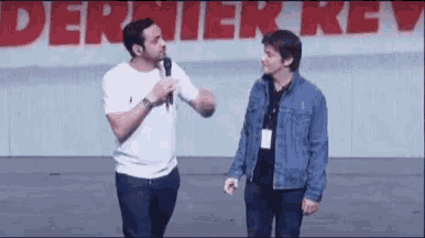 a man is talking into a microphone while another man stands behind him .