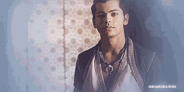 a man wearing a necklace and a white shirt with the words russarcreations on the bottom left