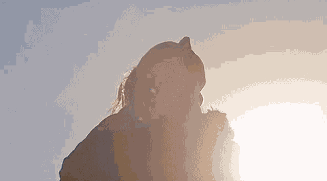 a woman is looking up at the sun while holding a flower in her hand .