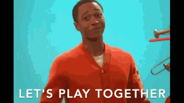 a man in an orange sweater says let 's play together while holding a trumpet