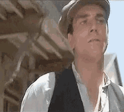 a man wearing a hat and vest is looking at something .
