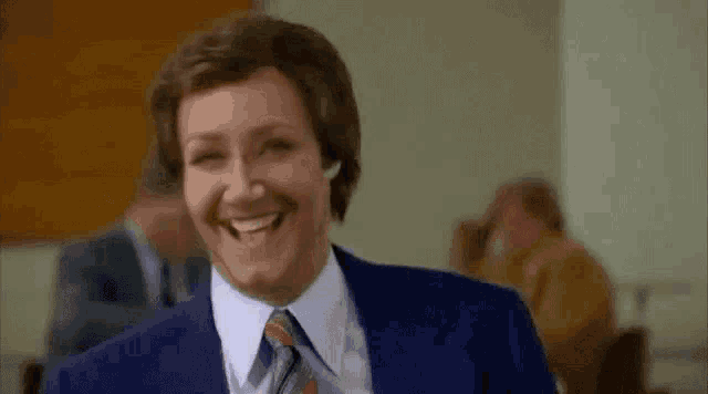 a man in a suit and tie is smiling in a room with other people .